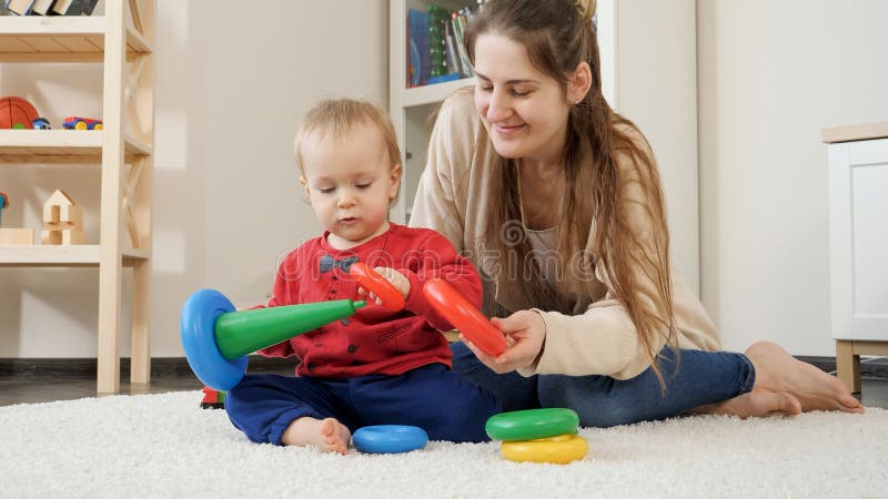 Cute little boy sitting with mother on carpet and playing with colorful toys. Baby development, child playing games, education and