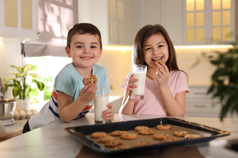 Little children eating cookies with milk in kitchen. Cooking pastry