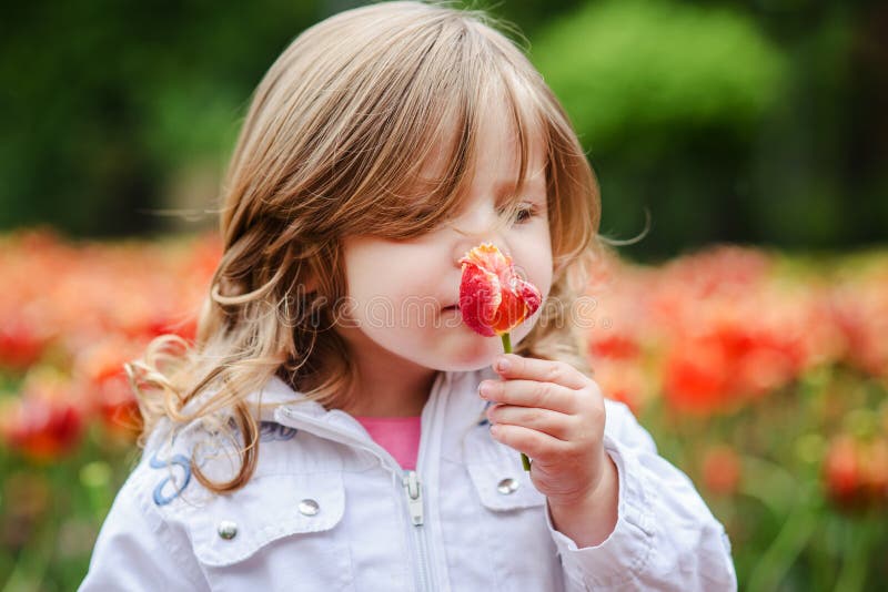 Cute little curly hair blonde girl smelling a tulip