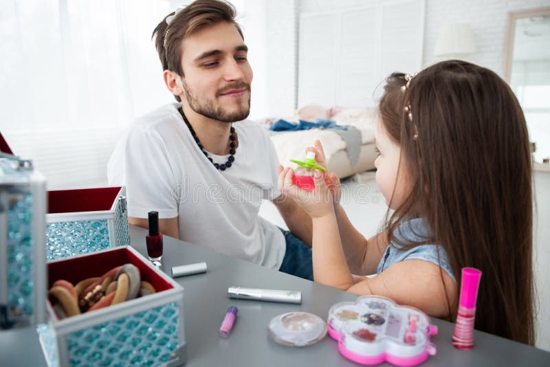 Cute little daughter and her handsome young dad in crowns are playing together in child`s room. Girl is doing her dad a royalty free stock photo Cute little daughter and her handsome young dad in crowns are playing together in child`s room. Girl is doing her dad a royalty free stock photo