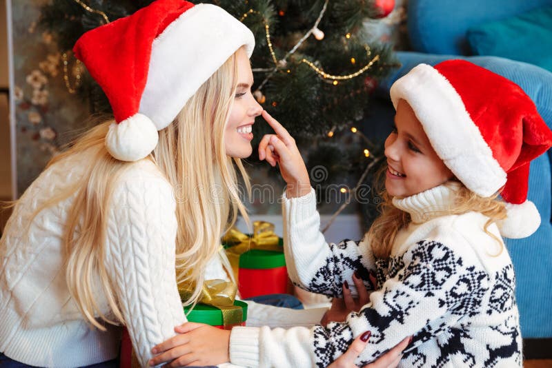 Cute little daughter in Santa`s hat touching nose of her smiling.