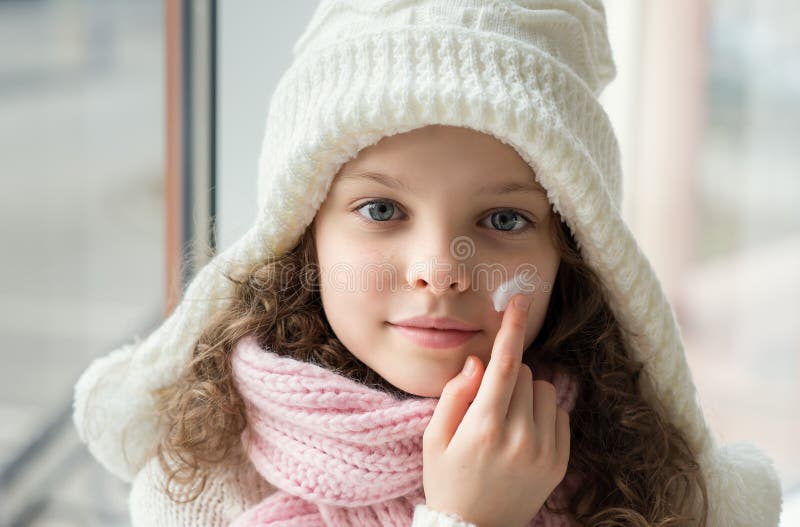 Cute little girl applying protecting cream to her face. Winter skin protection concept