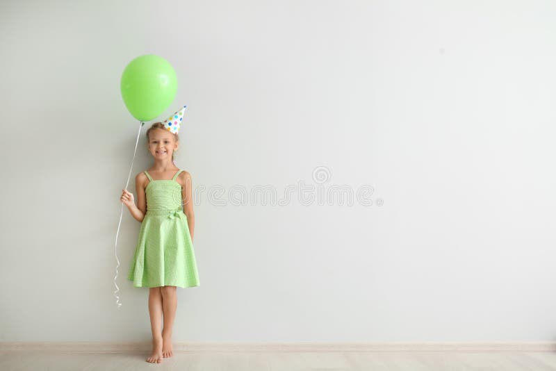 Cute little girl in Birthday hat and with balloon near light wall