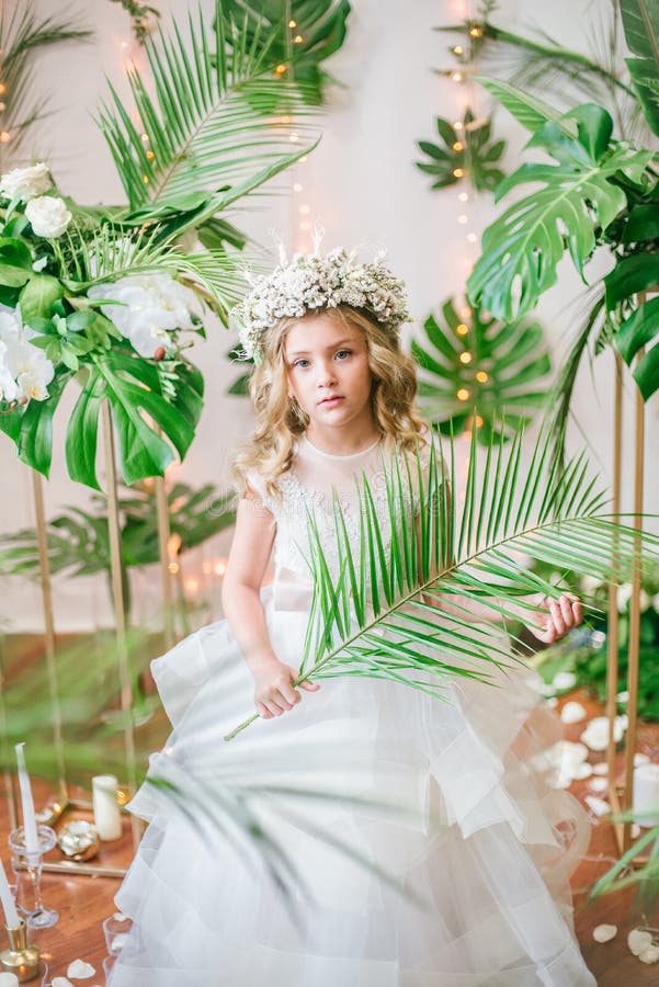 Cute little girl with blond curly hair in a white wedding dress and a wreath of flowers in floral decorations stock photography Cute little girl with blond curly hair in a white wedding dress and a wreath of flowers in floral decorations stock photography