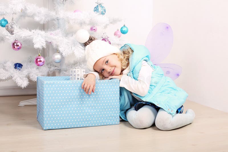 Cute little girl with blond hair posing beside a Christmas tree