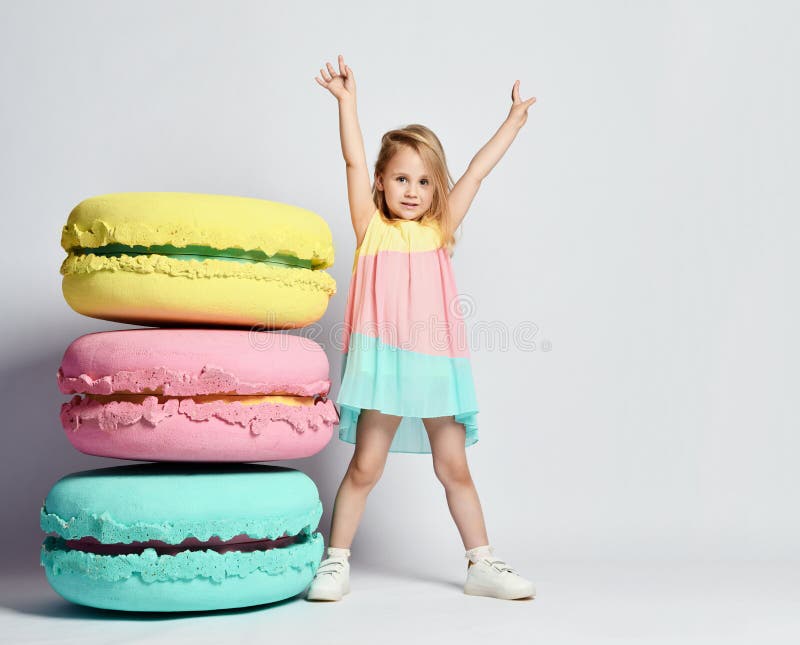 Cute little girl in bright clothes have fun at the birthday party fun room decoration candy macarons.