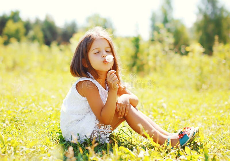 Cute little girl child blowing dandelion flower in sunny summer