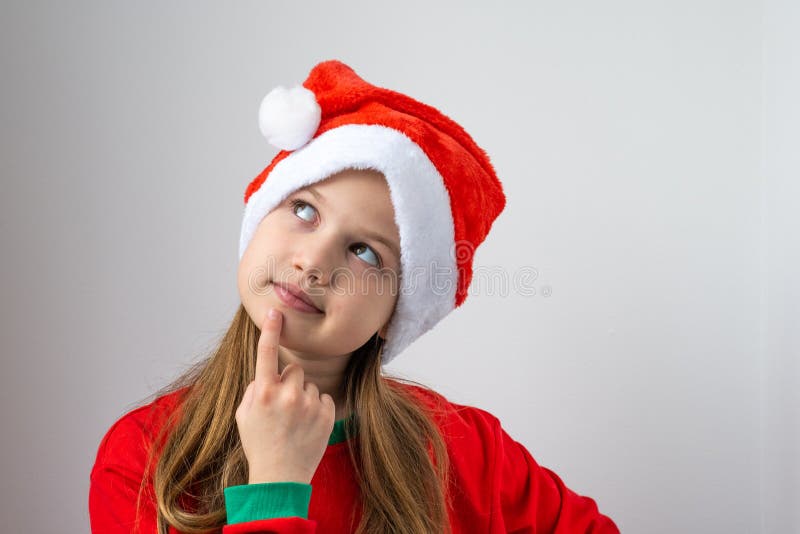 Cute little girl in Christmas red hat on white background thinking. Serious child looking up with doubtful and skeptical stock image
