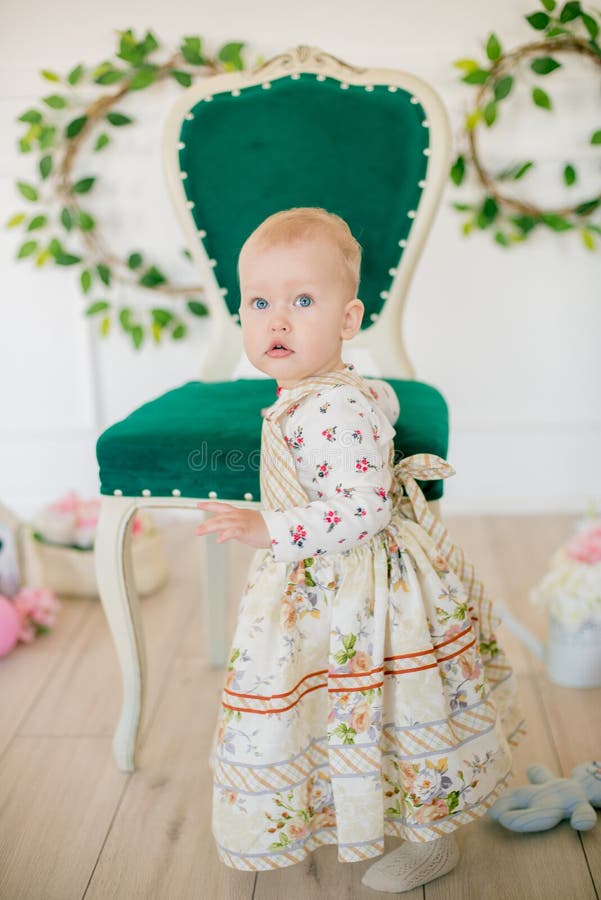 Cute little girl in a dress with a flower print in the Easter decorations in the studio. Little girl with easter eggs