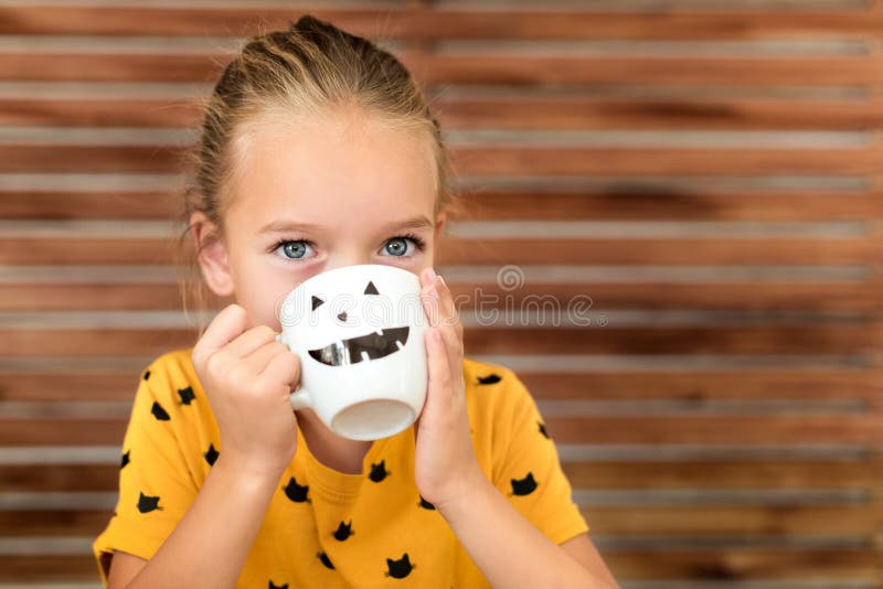 Cute little girl drinking pumpkin soup out of a cup with Halloween anthropomorphic smiley face. Autumn season comfort food. stock image Cute little girl drinking pumpkin soup out of a cup with Halloween anthropomorphic smiley face. Autumn season comfort food. stock image
