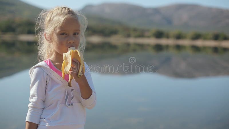 Cute little girl eating a banana while standing