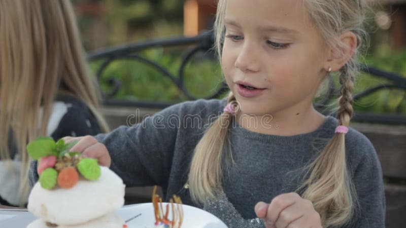 Cute little girl eating cake in the open air cafe