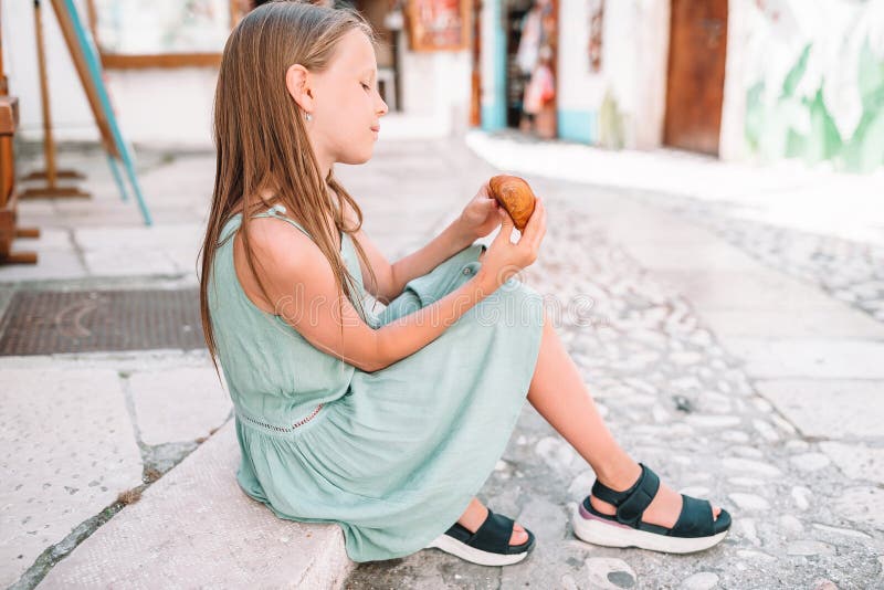Little girl eats croissant on old streets in european village royalty free stock photos
