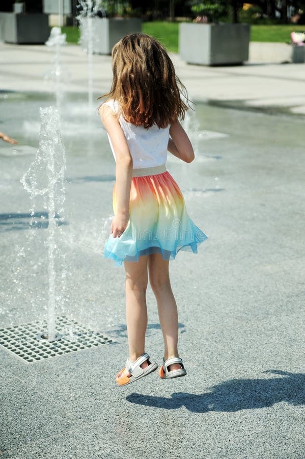 Cute little girl has fun near the fountain.