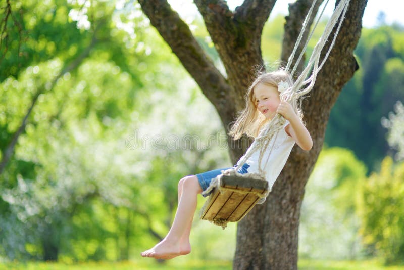 Cute little girl having fun on a swing in blossoming old apple tree garden outdoors on sunny spring day.