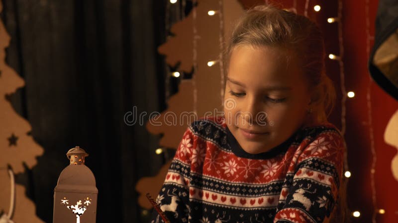 Cute little girl with a lantern writes a letter to Santa Claus on Christmas Eve in slow motion