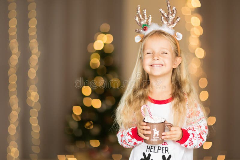 Cute Little girl with long blonde hair in christmas pajamas holding cup of cacao with marshmallow at home. Christmas decorations royalty free stock images Cute Little girl with long blonde hair in christmas pajamas holding cup of cacao with marshmallow at home. Christmas decorations royalty free stock images