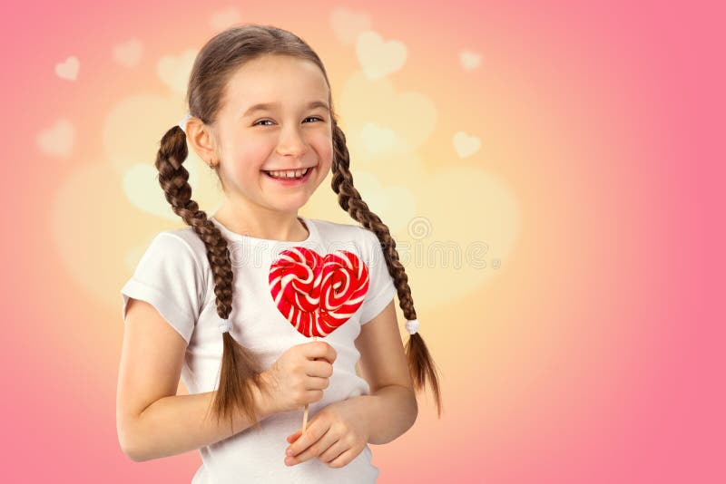Cute little girl in love with candy lollipop heart on pink background. Valentine`s day.