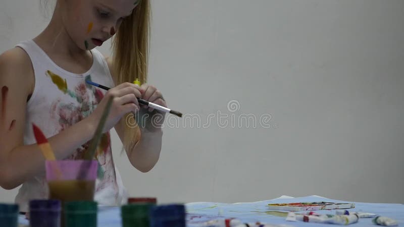 Cute little girl painter draws on the table and on himself on her clothes. slow motion