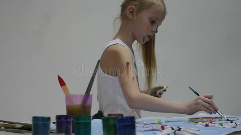 Cute little girl painter draws on the table and on himself on her clothes. slow motion