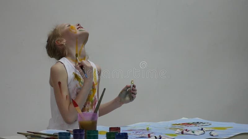 Cute little girl painter draws on the table and on himself on her clothes. slow motion