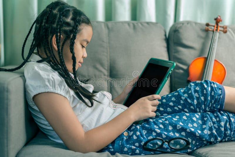 Cute little girl,playing with computer at home laying on sofa
