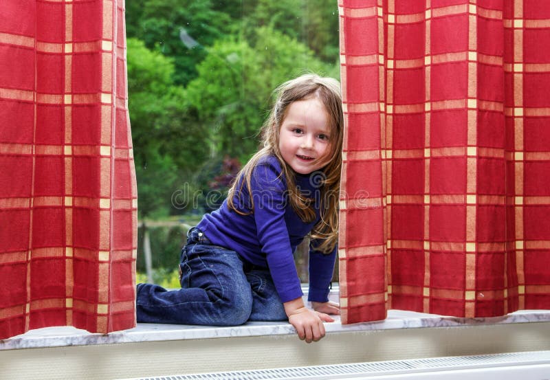 Cute little girl playing with drapes on the window royalty free stock image