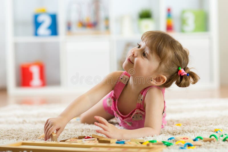 Cute little girl playing with educational toy blocks in a sunny kindergarten room. Kids playing. Children at day care.