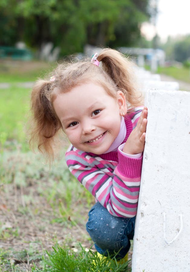 Cute little girl is playing hide and seek outdoors