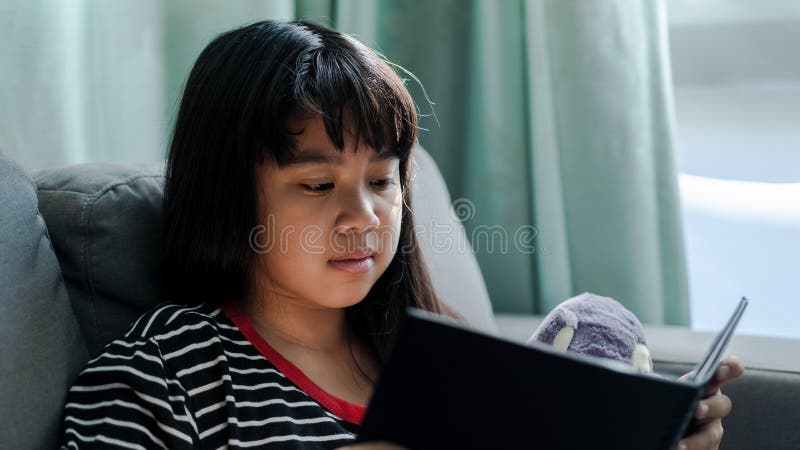Cute little girl reading book her doll at home stock photo Cute little girl reading book her doll at home stock photo