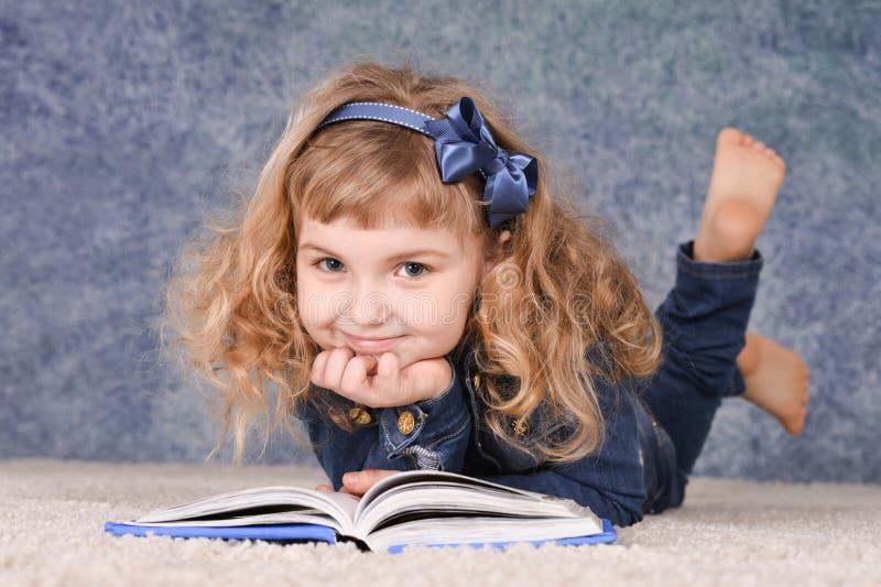 Cute little girl reading book while lying on floor