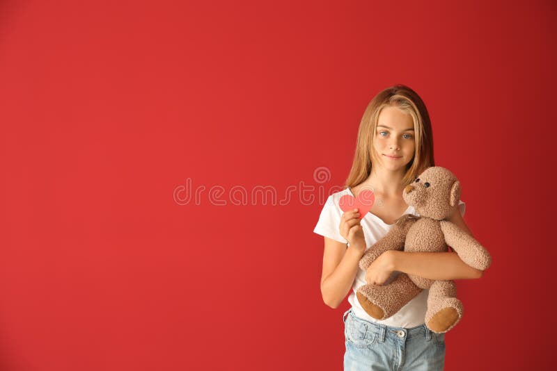 Cute little girl with red heart and teddy bear on color background