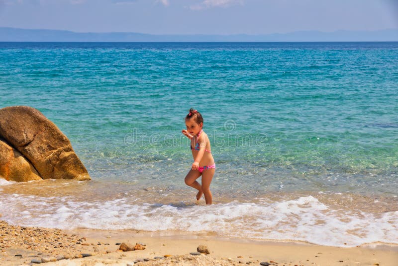 Cute little girl running at the beach near the sea on vacations