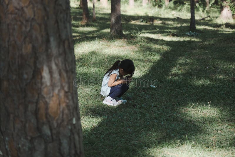 Cute little girl sits on the grass with her eyes closed while playing hide and seek with her family in the park. Happy child spending time with her family on vacation