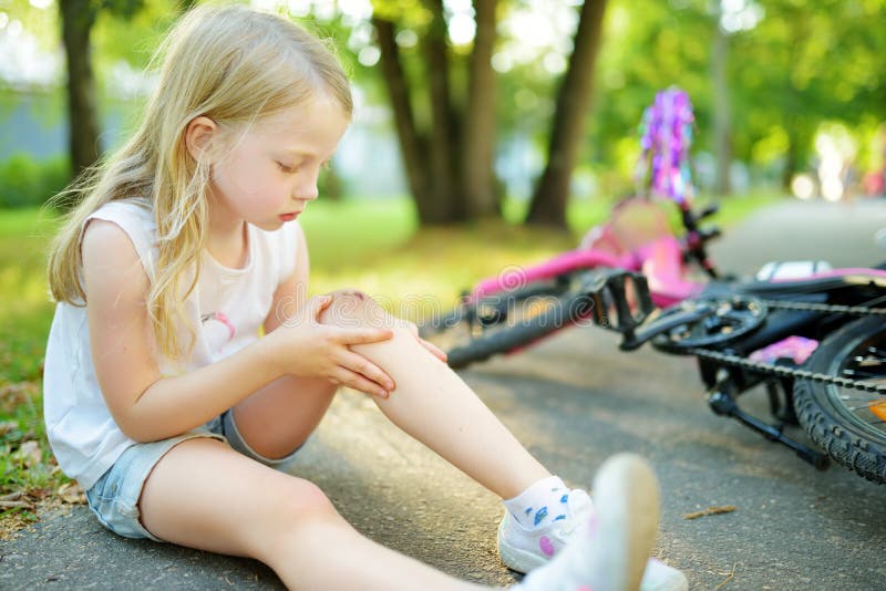 Cute little girl sitting on the ground after falling off her bike at summer park. Child getting hurt while riding a bicycle stock photography Cute little girl sitting on the ground after falling off her bike at summer park. Child getting hurt while riding a bicycle stock photography