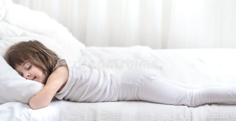 Cute little girl smiling while lying in a cozy white bed