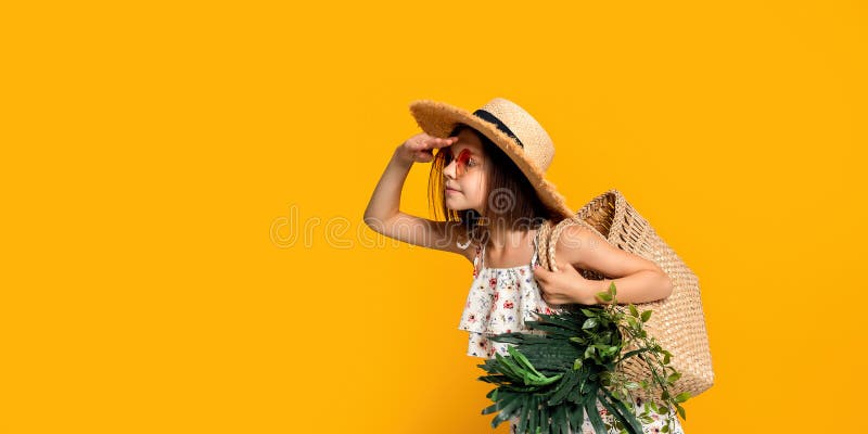 Cute little girl in straw hat in sunglasses holds handbag with tropical plants looking something