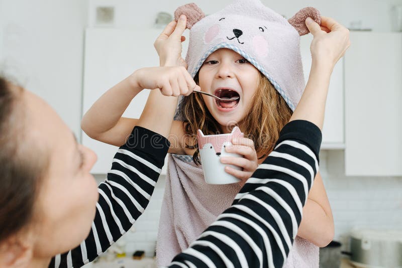 Cute little girl wrapped eating yogurt, while her mom playing with her bear hood