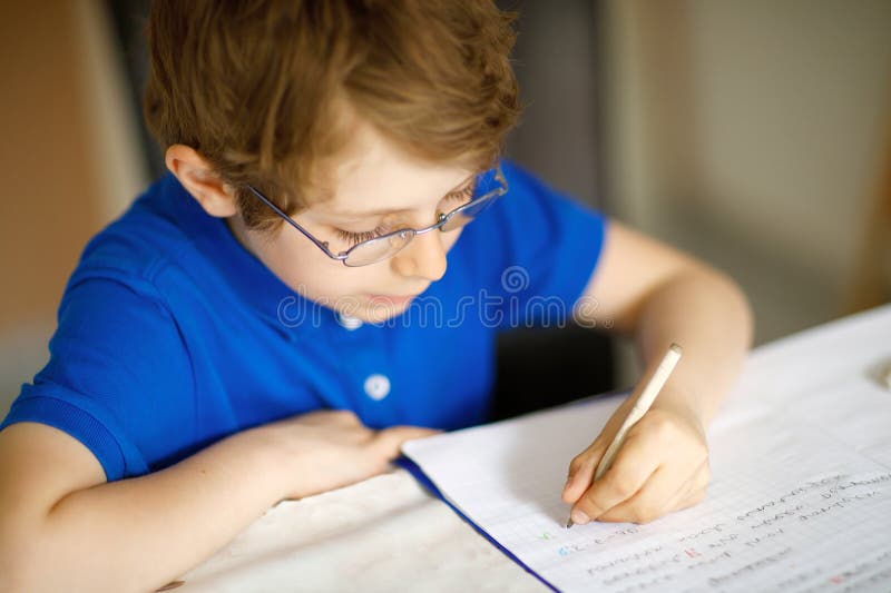 Cute little kid boy with glasses at home making homework, writing letters with colorful pens.