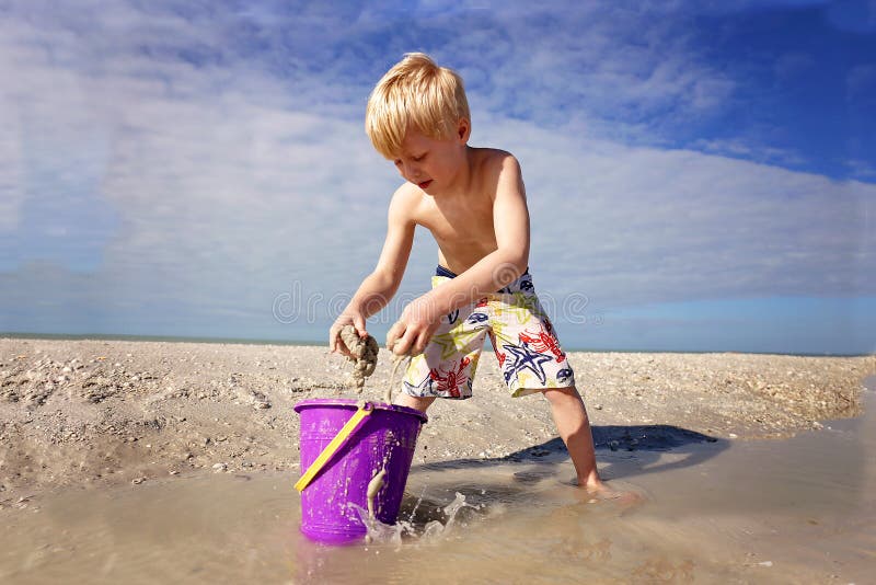 Cute Little Kid Playing with Sand in a Bucket at the Beach by the Ocean