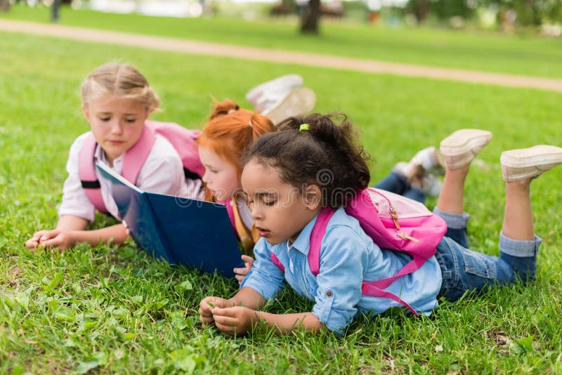 Multiethnic kids reading book on grass royalty free stock image Multiethnic kids reading book on grass royalty free stock image