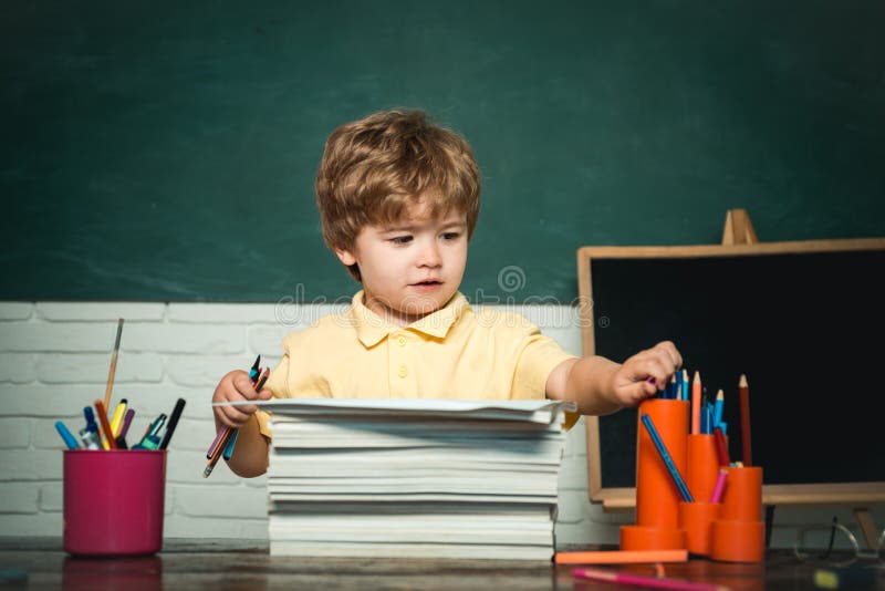 Cute little preschool kid boy study in a classroom. Funny little kid pointing up on blackboard - school concept. Kid is. Learning in class on background of royalty free stock photography Cute little preschool kid boy study in a classroom. Funny little kid pointing up on blackboard - school concept. Kid is. Learning in class on background of royalty free stock photography