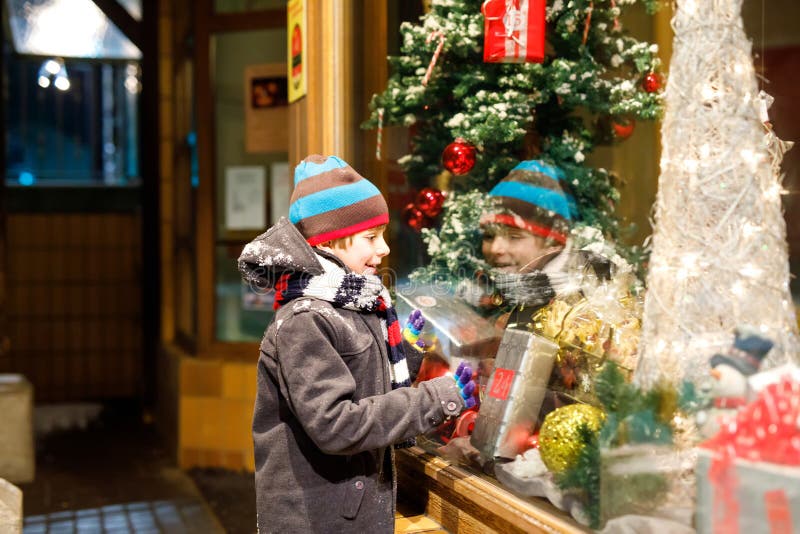 Funny happy child in fashion winter clothes making window shopping decorated with gifts, xmas tree stock images Funny happy child in fashion winter clothes making window shopping decorated with gifts, xmas tree stock images