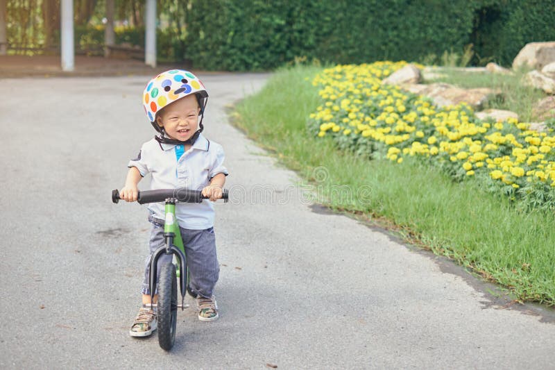 Cute little toddler boy child wearing safety helmet learning to ride first balance bike in sunny summer day, kid cycling at park