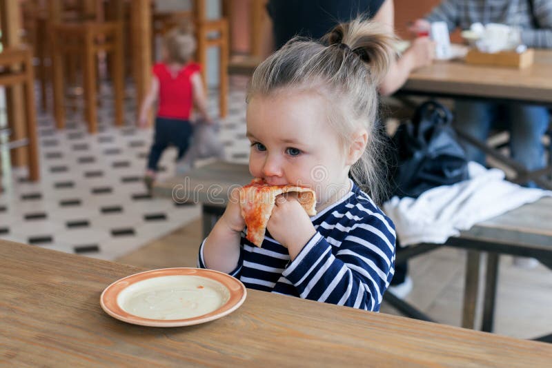 Cute little 2 years girl eating pizza in the restaurant.