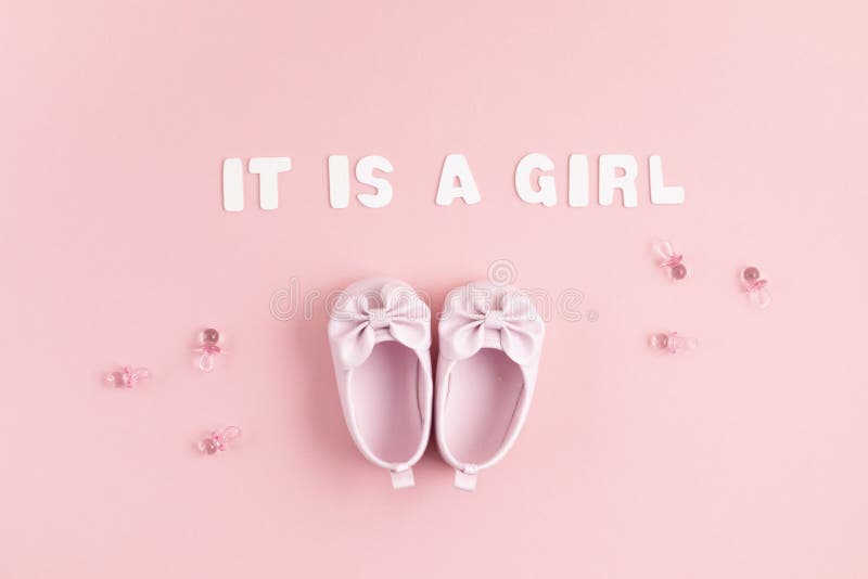 Cute newborn baby girl shoes with festive decoration over pink background. Baby shower, birthday, invitation or greeting card. Idea
