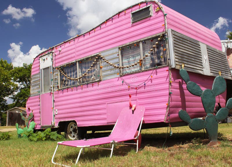 Cute pink travel trailer under a bright cloudy sky with cacti and trees around a tumbona chair stock photos