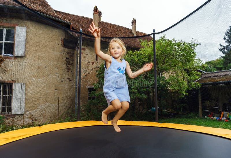 Cute preschooler girl jumping on trampoline.