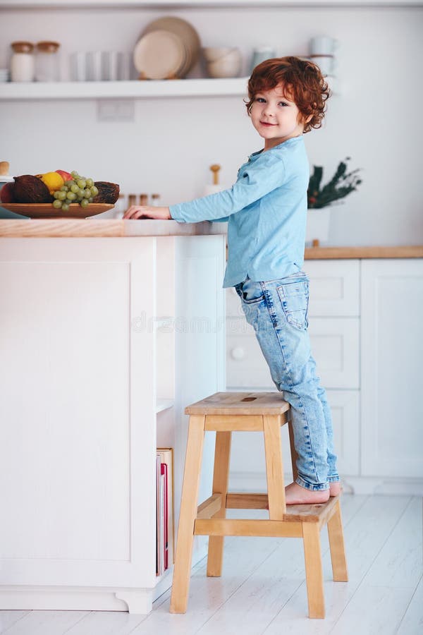Cute redhead kid, boy standing on step stool in the kitchen