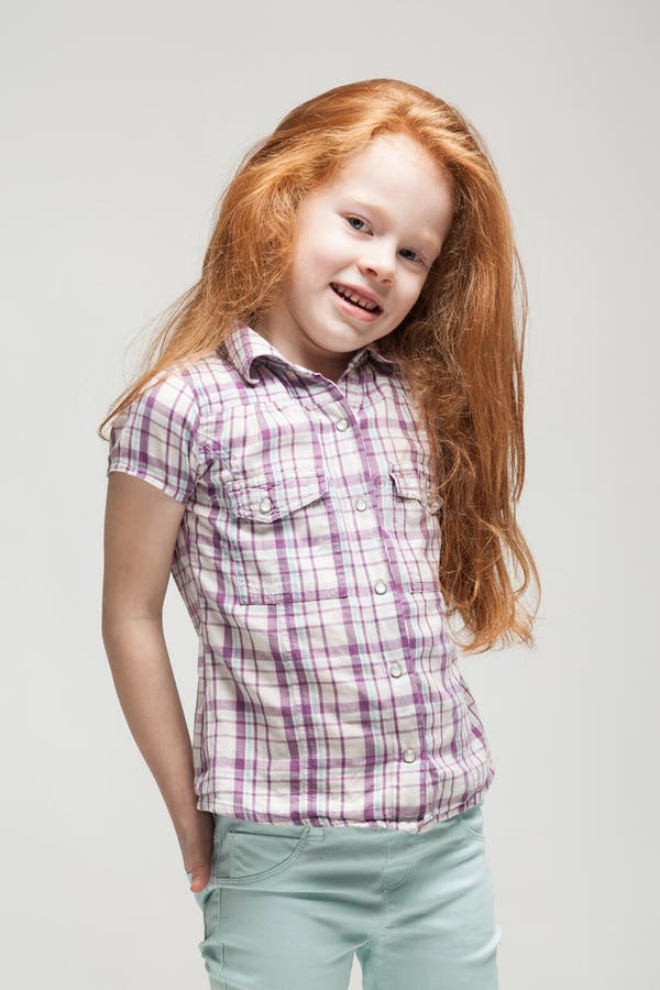 Cute redhead little girl in plaid shirt, bright blue trousers and white boots